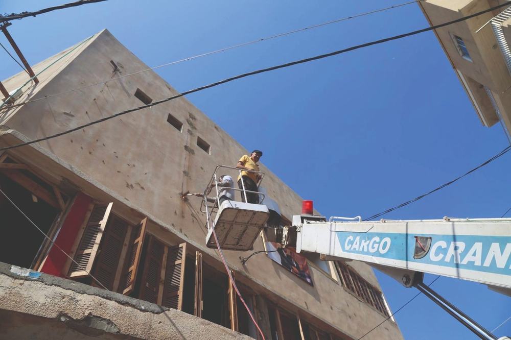 A worker on a crane platform repairing Le Colisée's facade