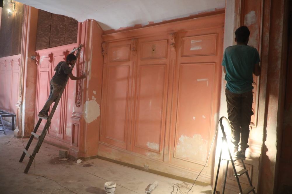 Two workers on ladders repairing the panelled walls of Le Colisée's hall